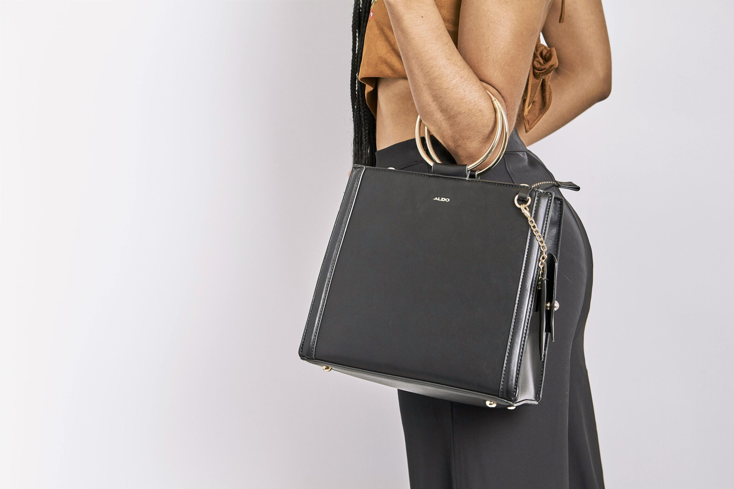A fashionable woman holding a chic black leather handbag against a white background, showcasing style and elegance.